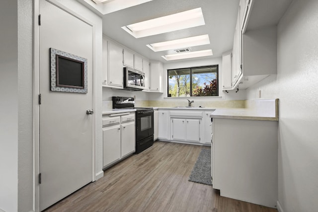 kitchen featuring light countertops, light wood-style flooring, stainless steel microwave, a sink, and electric range