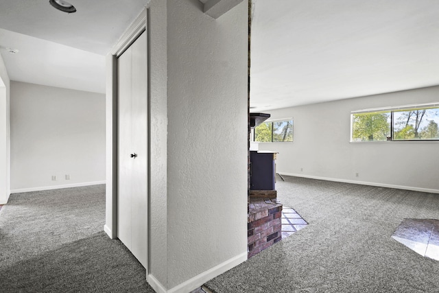hall featuring carpet flooring, a textured wall, and baseboards