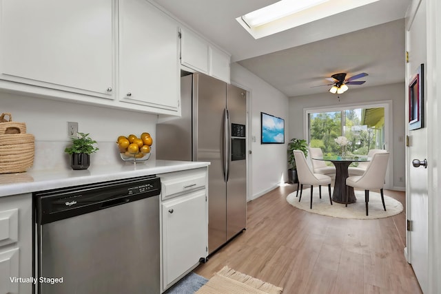 kitchen with light countertops, white cabinetry, a skylight, appliances with stainless steel finishes, and light wood-style flooring