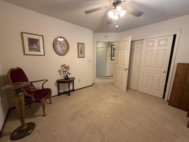 living area featuring baseboards, a textured ceiling, ceiling fan, and light carpet