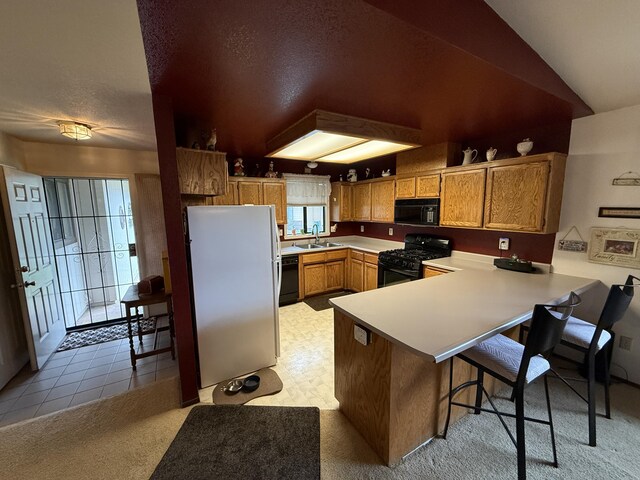 kitchen featuring light countertops, a sink, a breakfast bar area, a peninsula, and black appliances