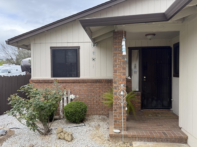 doorway to property featuring brick siding and fence