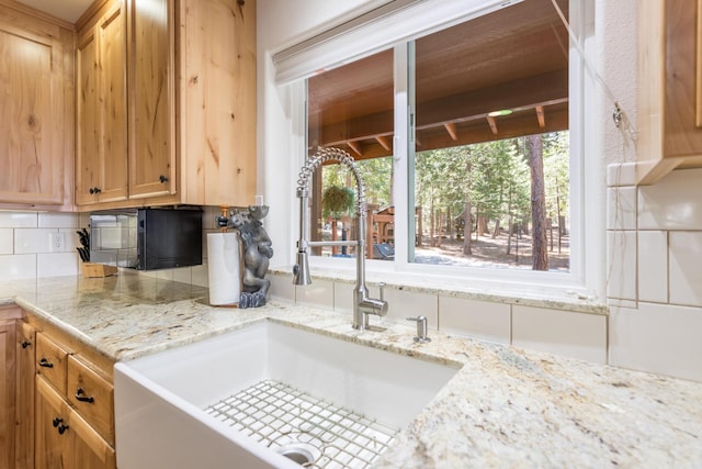kitchen featuring decorative backsplash, a wealth of natural light, a sink, and light stone countertops