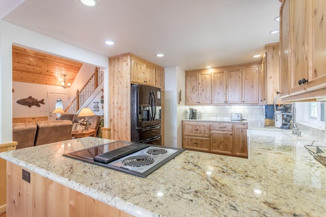 kitchen with black refrigerator with ice dispenser, stovetop with downdraft, light brown cabinetry, decorative backsplash, and light stone countertops