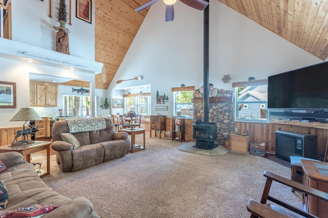carpeted living room with wooden walls, wainscoting, a ceiling fan, a wood stove, and wood ceiling