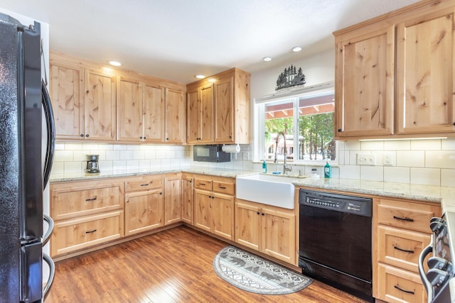 kitchen featuring a sink, black appliances, wood finished floors, and light brown cabinetry
