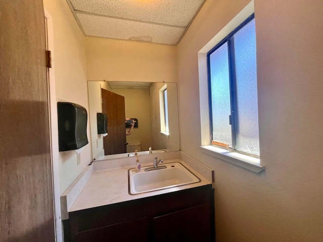 bathroom featuring toilet, vanity, and a drop ceiling