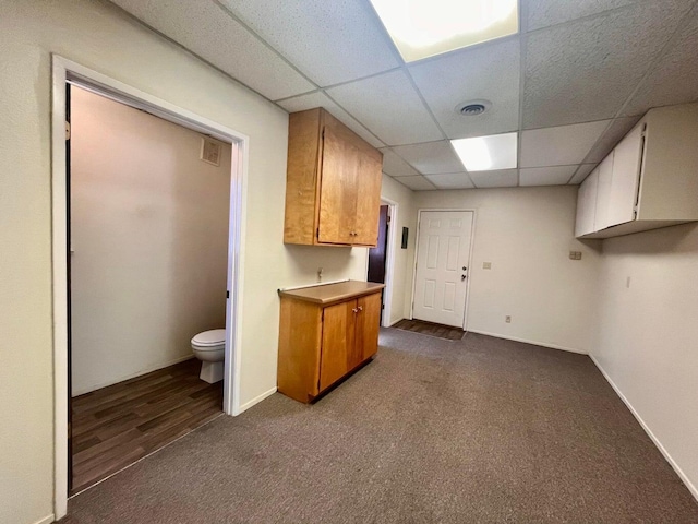 kitchen featuring baseboards, a drop ceiling, dark carpet, visible vents, and brown cabinets