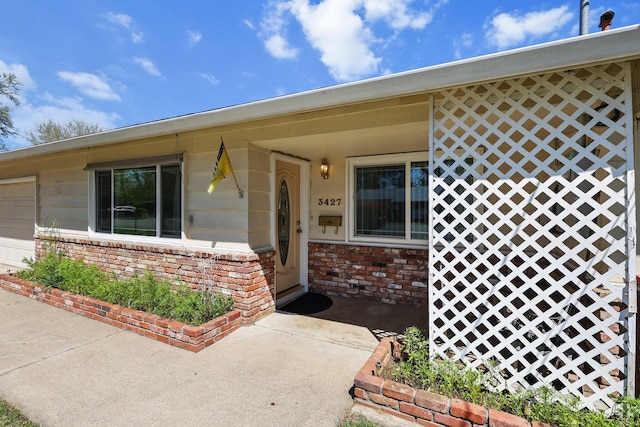 view of exterior entry with an attached garage and brick siding