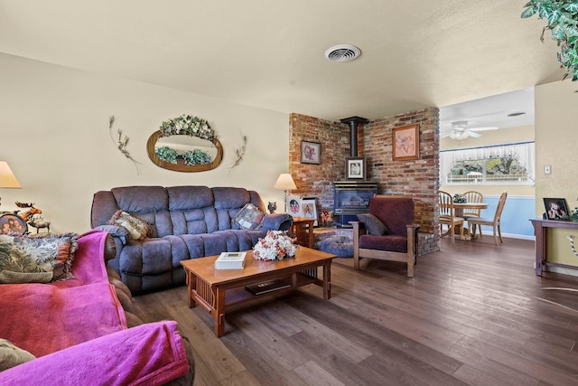 living room with baseboards, a wood stove, visible vents, ceiling fan, and wood finished floors