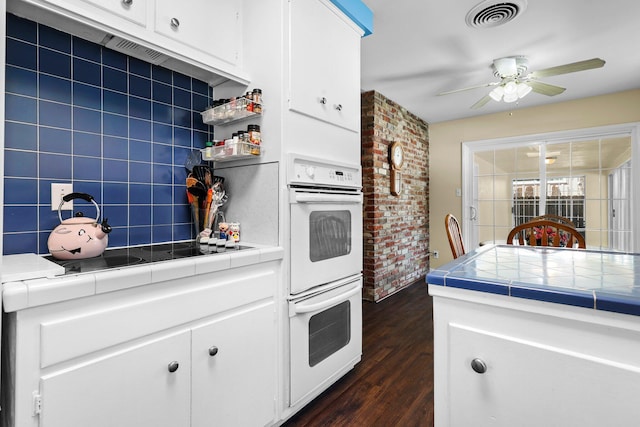 kitchen with tile countertops, dark wood-type flooring, a ceiling fan, white cabinets, and visible vents