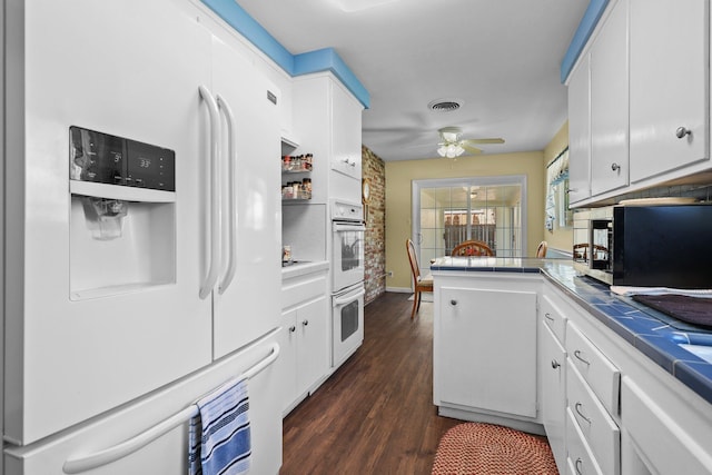 kitchen featuring white appliances, white cabinetry, a ceiling fan, visible vents, and tile countertops