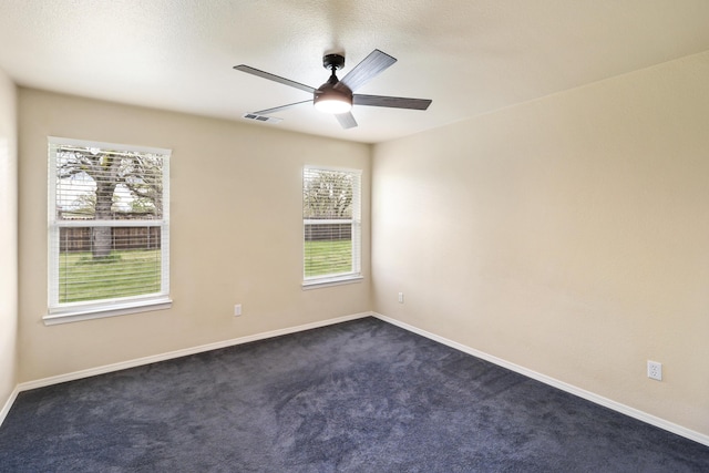 spare room with baseboards, visible vents, ceiling fan, and dark carpet