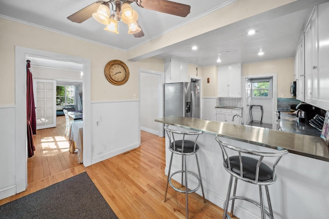 kitchen with stainless steel appliances, white cabinets, ceiling fan, light wood-type flooring, and a peninsula