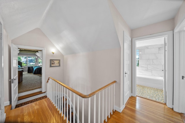 hall featuring baseboards, wood finished floors, an upstairs landing, and lofted ceiling