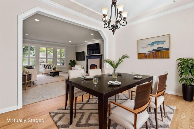 dining space featuring ornamental molding, a fireplace, light wood-type flooring, baseboards, and a chandelier