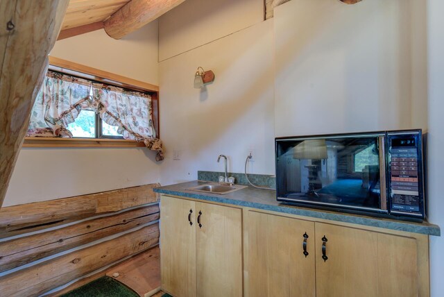 kitchen featuring lofted ceiling, light brown cabinets, a sink, black microwave, and dark countertops