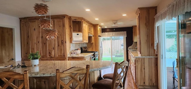 kitchen featuring stainless steel gas range, recessed lighting, light stone countertops, a breakfast bar, and a ceiling fan
