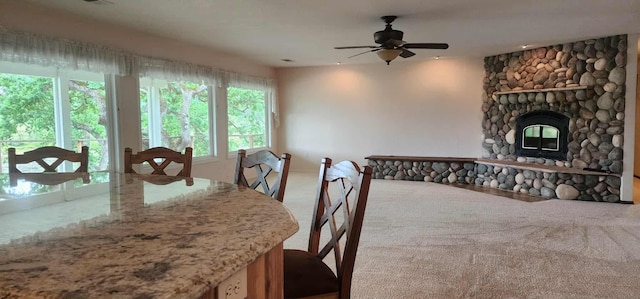 carpeted dining area featuring ceiling fan and a stone fireplace