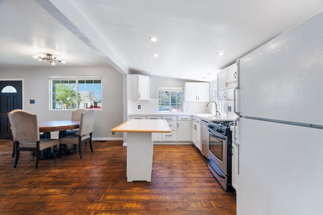 kitchen with lofted ceiling with beams, light countertops, freestanding refrigerator, dark wood finished floors, and stainless steel gas range oven