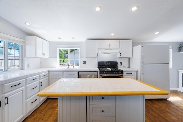 kitchen with dishwasher, freestanding refrigerator, under cabinet range hood, tile counters, and black gas range oven