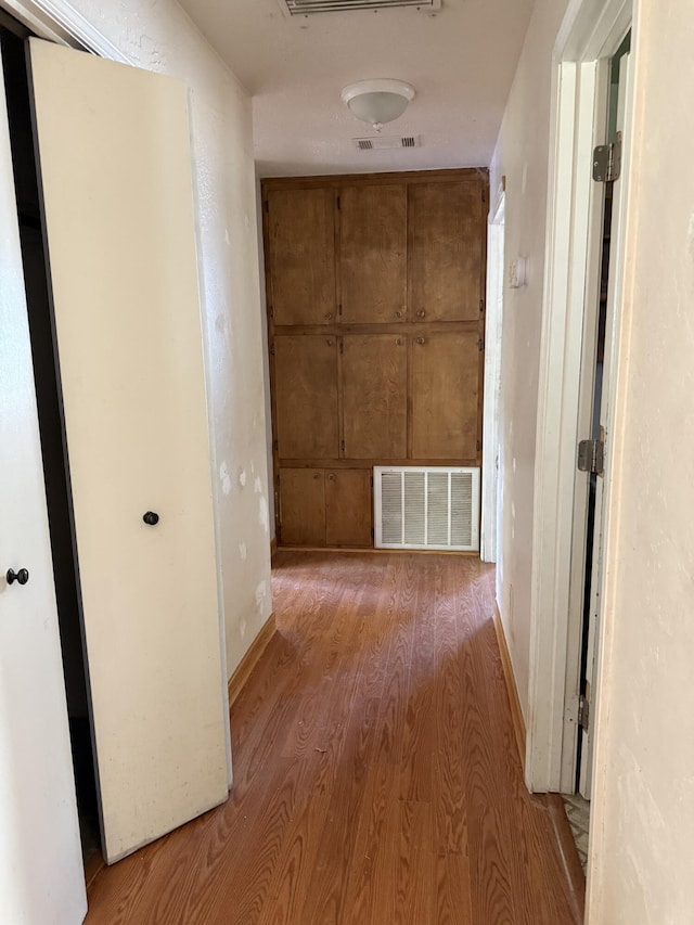 hall featuring baseboards, visible vents, and wood finished floors