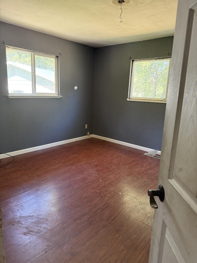 empty room with baseboards, a wealth of natural light, and dark wood-type flooring