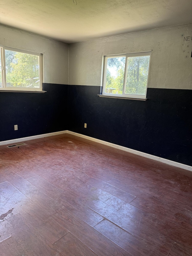 unfurnished room featuring wood-type flooring, visible vents, and baseboards