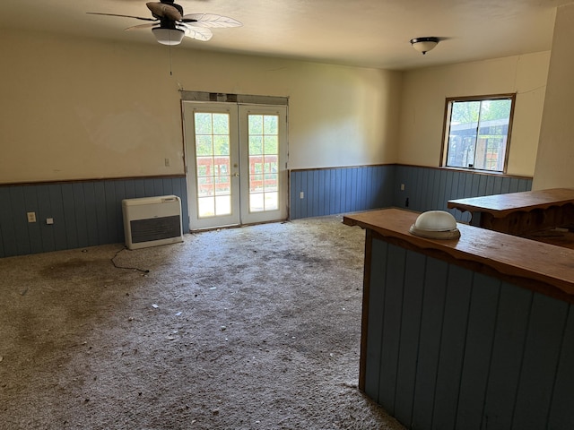 interior space with a ceiling fan, heating unit, a wainscoted wall, and french doors