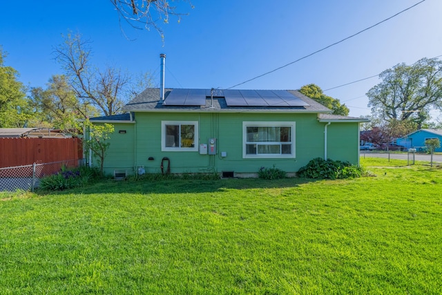 back of house with roof mounted solar panels and a shingled roof