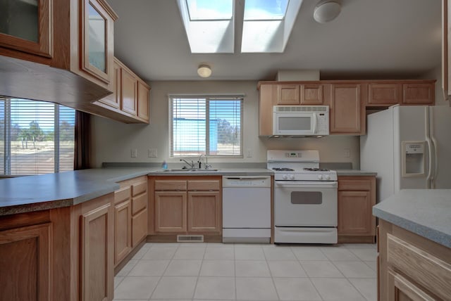 kitchen featuring a skylight, light brown cabinets, white appliances, and a sink