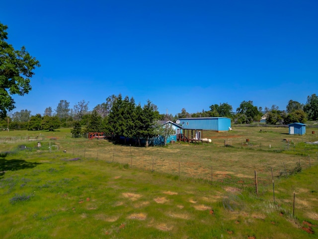 view of yard featuring fence, an outdoor structure, and a rural view