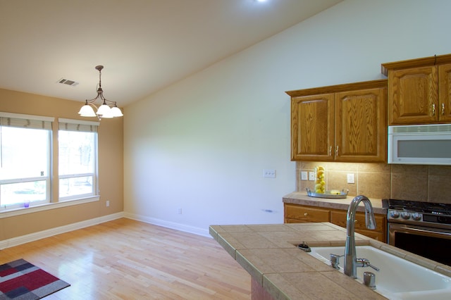 kitchen with visible vents, a sink, light wood-style floors, white microwave, and lofted ceiling