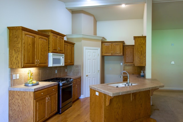 kitchen with a sink, a peninsula, brown cabinetry, white microwave, and stainless steel gas stove