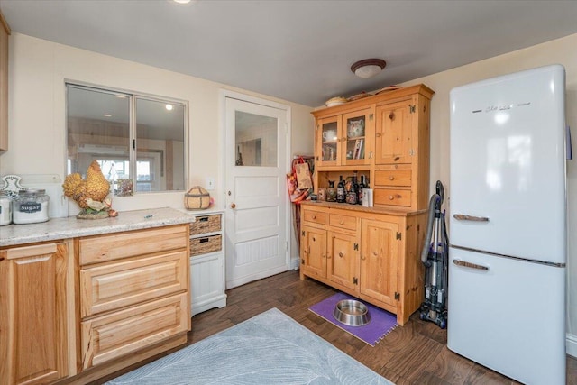 kitchen with glass insert cabinets, freestanding refrigerator, light stone counters, and dark wood finished floors