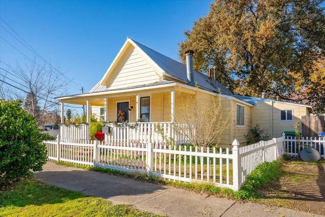 farmhouse inspired home featuring a porch, a fenced front yard, and metal roof
