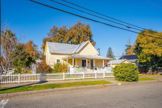 farmhouse featuring a porch, metal roof, and a fenced front yard