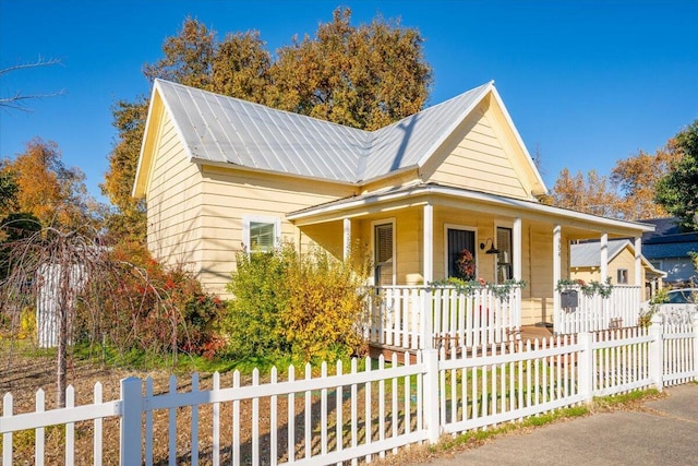 farmhouse inspired home with a porch, metal roof, and a fenced front yard