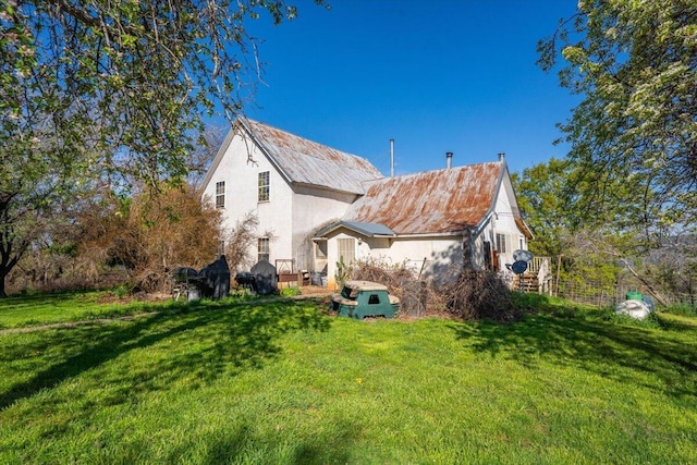 back of house featuring a yard, metal roof, and stucco siding
