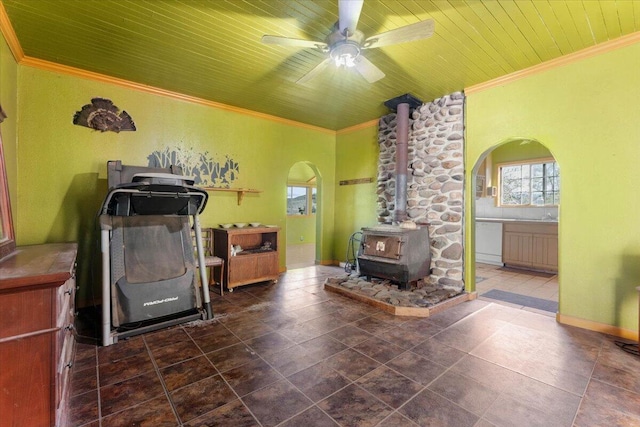 interior space with ornamental molding, a wood stove, ceiling fan, arched walkways, and wood ceiling