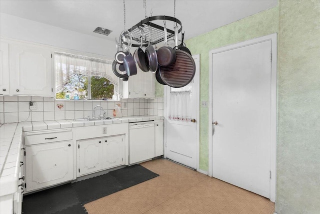 kitchen featuring tile counters, white cabinets, light floors, dishwasher, and a sink