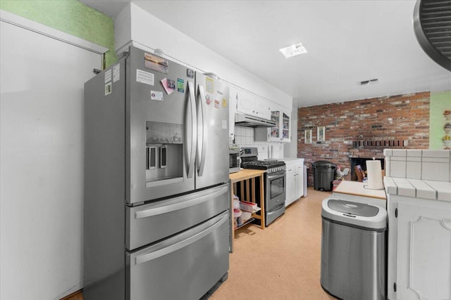 kitchen featuring white cabinets, under cabinet range hood, light floors, stainless steel appliances, and tile countertops