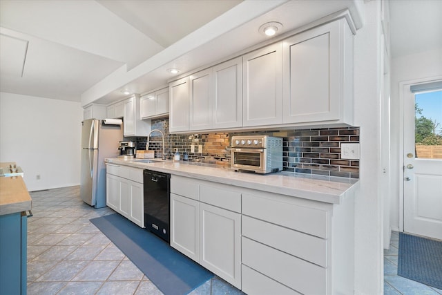 kitchen with a sink, black dishwasher, freestanding refrigerator, and tasteful backsplash