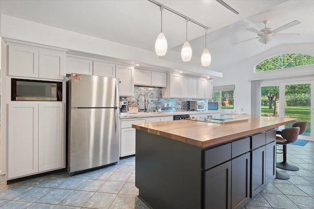 kitchen with backsplash, vaulted ceiling, a sink, butcher block counters, and stainless steel appliances