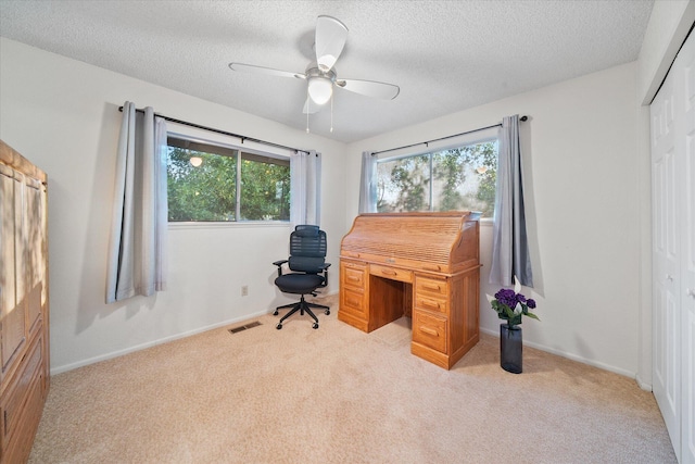 office featuring a ceiling fan, a textured ceiling, visible vents, baseboards, and light carpet