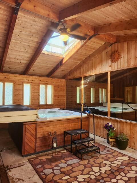 interior space with a skylight, a hot tub, and beam ceiling