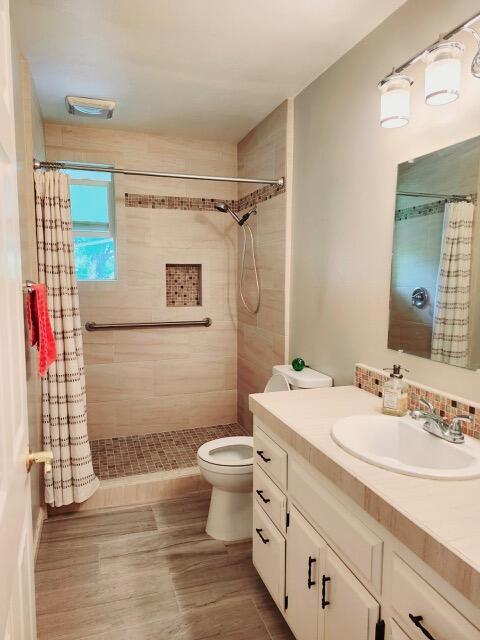 bathroom with vanity, visible vents, wood finished floors, toilet, and a tile shower