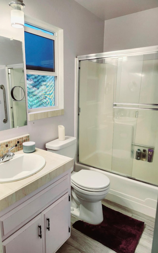 bathroom featuring shower / bath combination with glass door, wood finished floors, toilet, and vanity