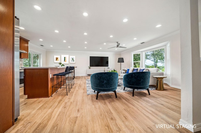 living area with a healthy amount of sunlight, ornamental molding, light wood-style flooring, and a ceiling fan