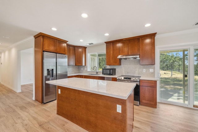 kitchen with under cabinet range hood, appliances with stainless steel finishes, light wood-type flooring, and a sink